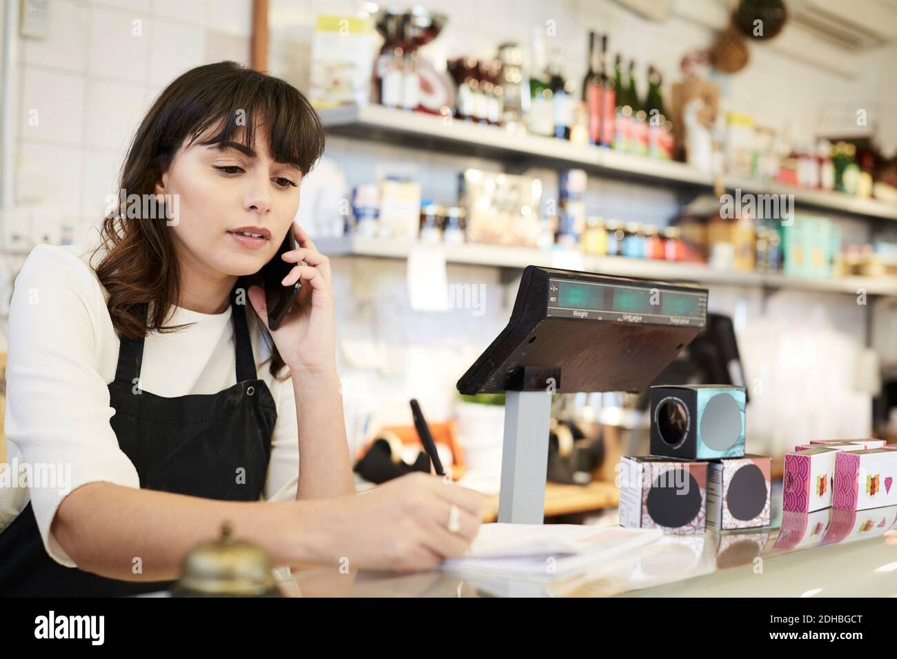 Femme propriétaire prenant la commande par téléphone portable au comptoir à l'intérieur stocker Banque D'Images