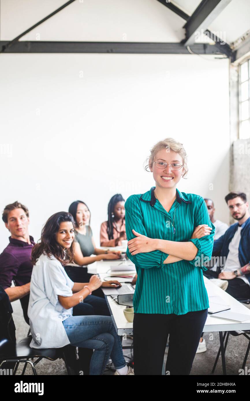 Portrait d'une femme souriante hacker informatique avec les bras croisés debout contre l'équipe sur le lieu de travail Banque D'Images