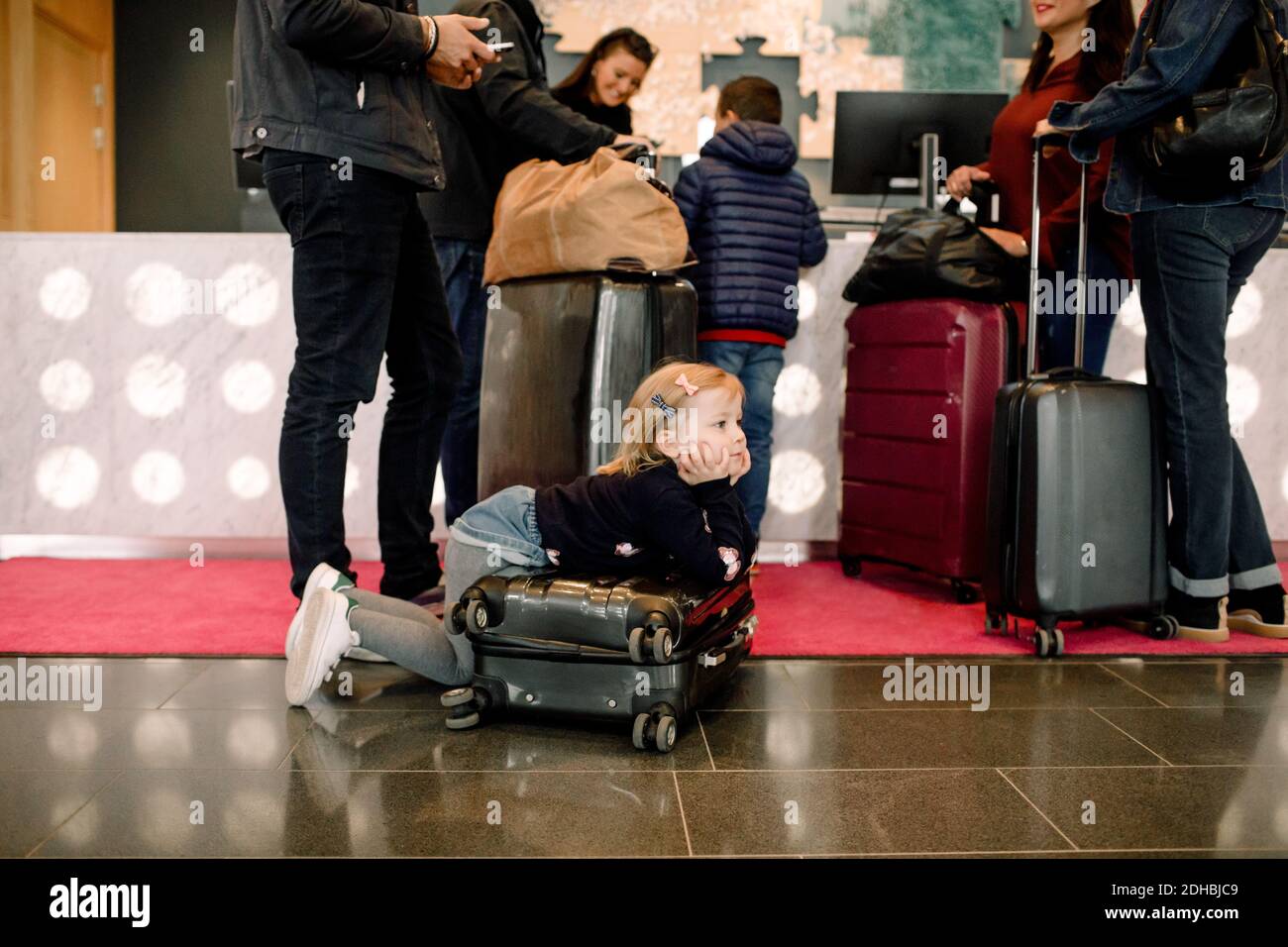 Ennui fille regardant loin en se penchant sur la valise avec la famille debout à la réception de l'hôtel Banque D'Images