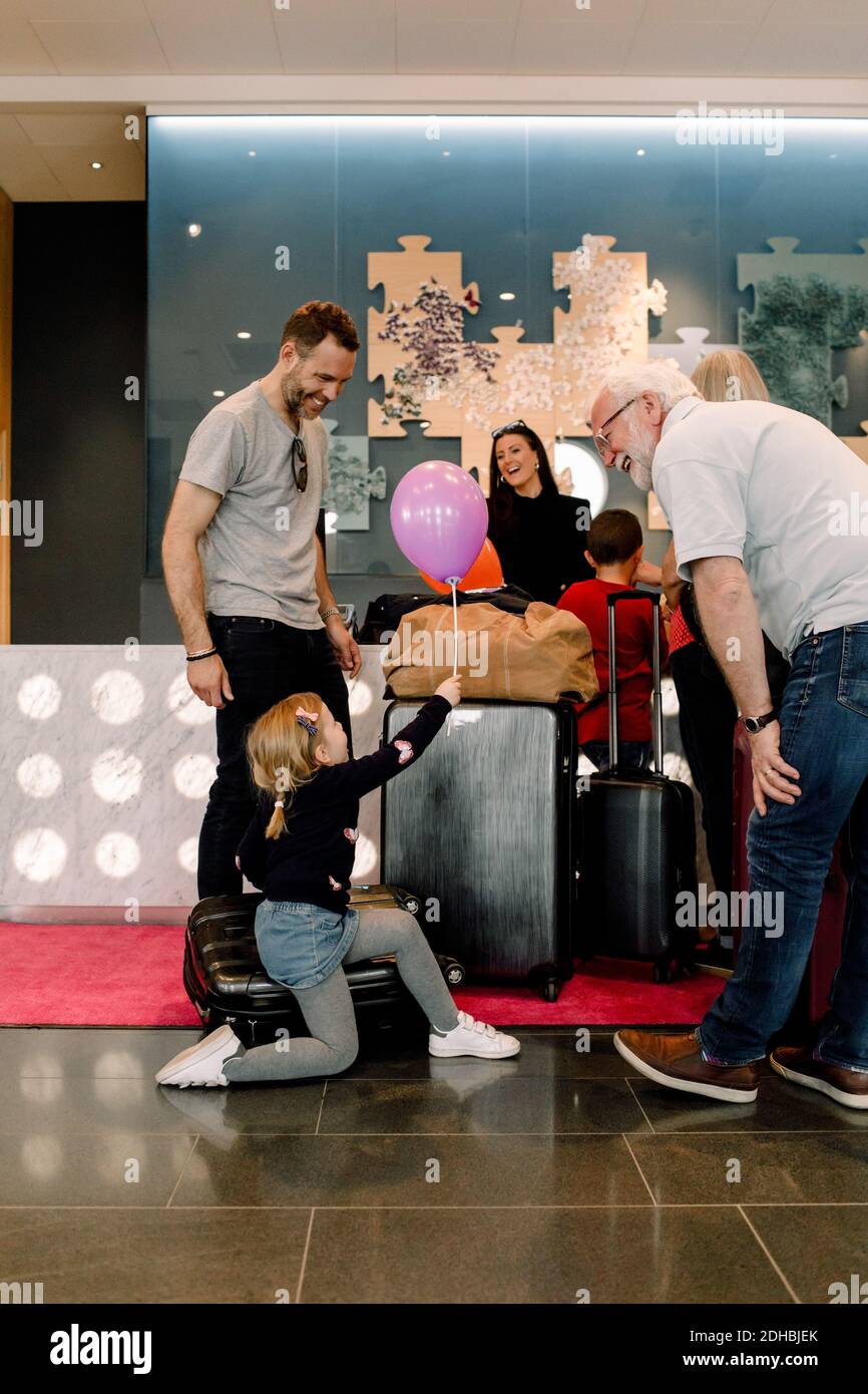 Parents regardant une fille tenant un ballon tout en étant assis sur une valise dans l'hôtel Banque D'Images