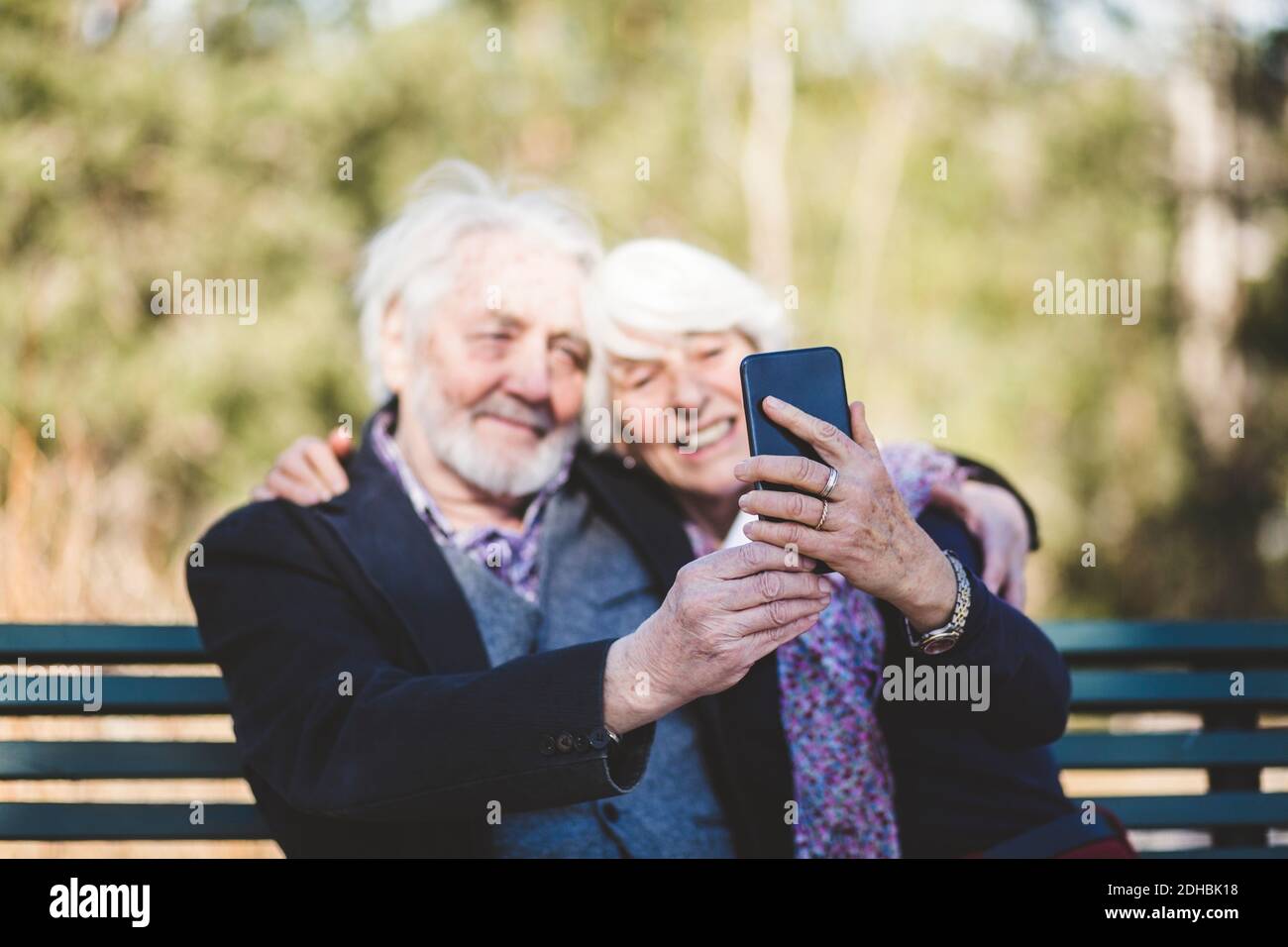 Couple senior souriant prenant le selfie assis sur le banc Banque D'Images