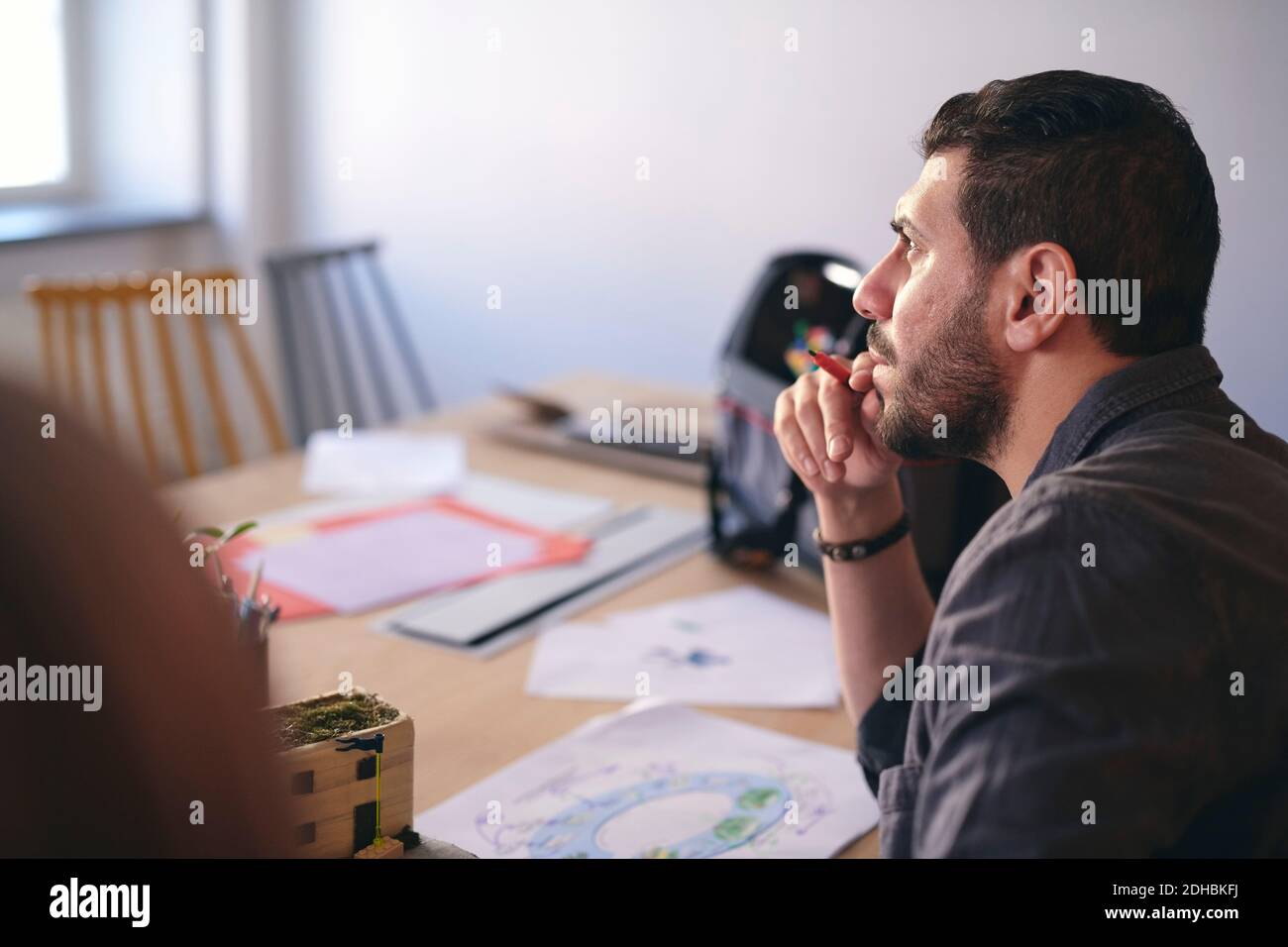 Vue latérale d'un ingénieur en train de penser tout en étant assis avec le schéma à la table dans le bureau Banque D'Images