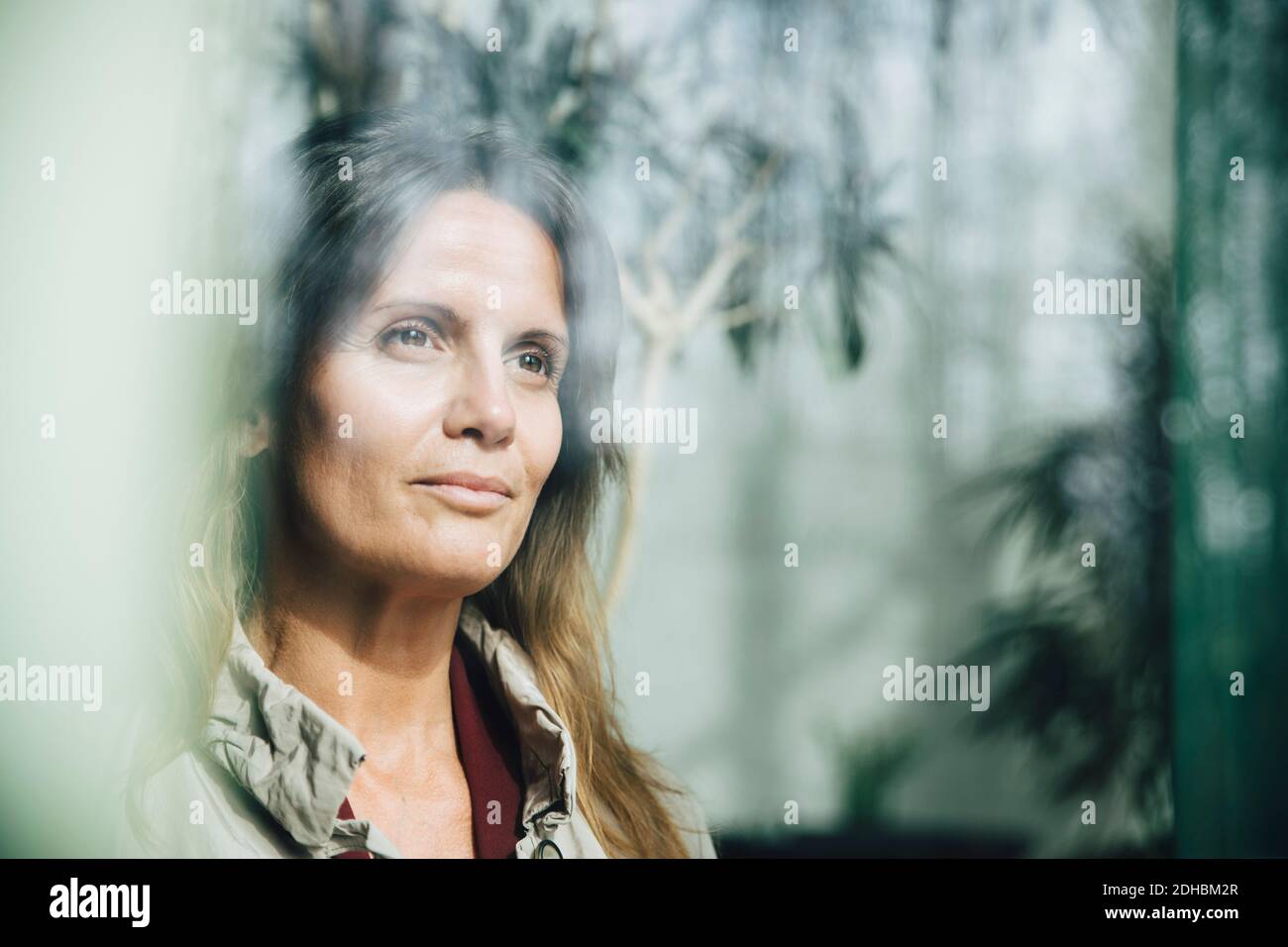 Femme d'affaires mûre et réfléchie regardant par la fenêtre au bureau Banque D'Images