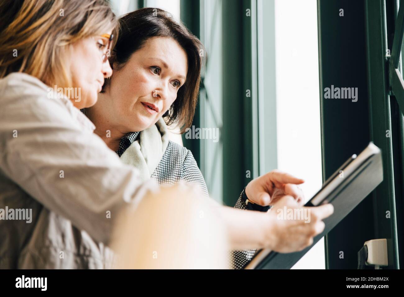 Femme d'affaires confiante et mature qui pointe vers le document tout en planifiant avec une femme collègue au bureau Banque D'Images