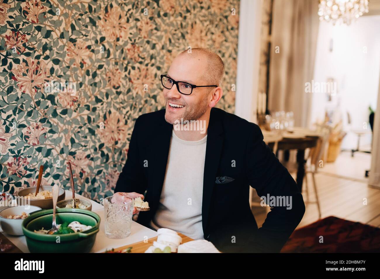 Homme mûr souriant regardant loin tout en étant assis avec la nourriture à tableau Banque D'Images