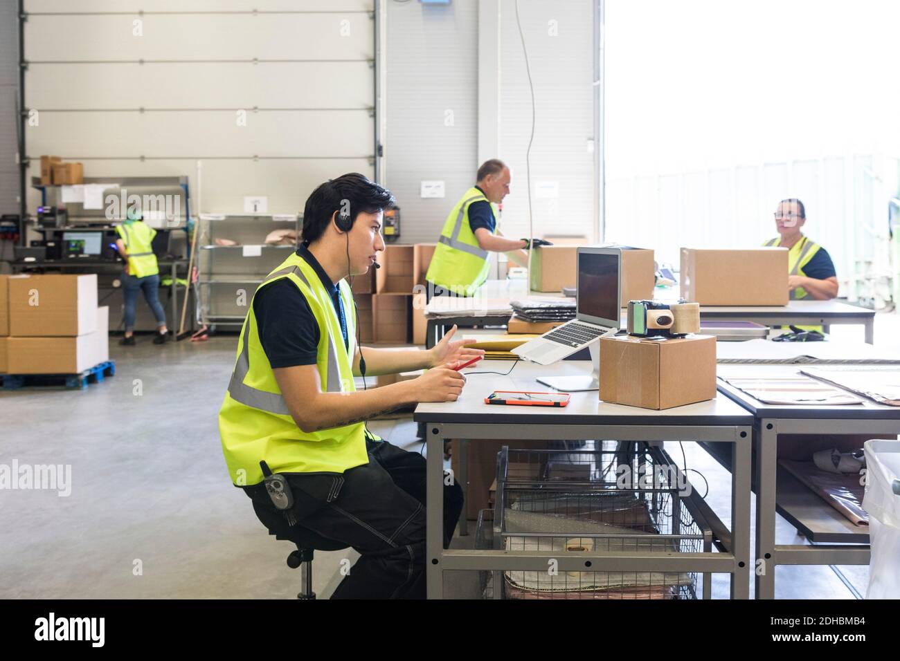 Un jeune représentant du service clientèle parle avec son micro-casque pendant que ses collègues se sont rendus à entrepôt Banque D'Images