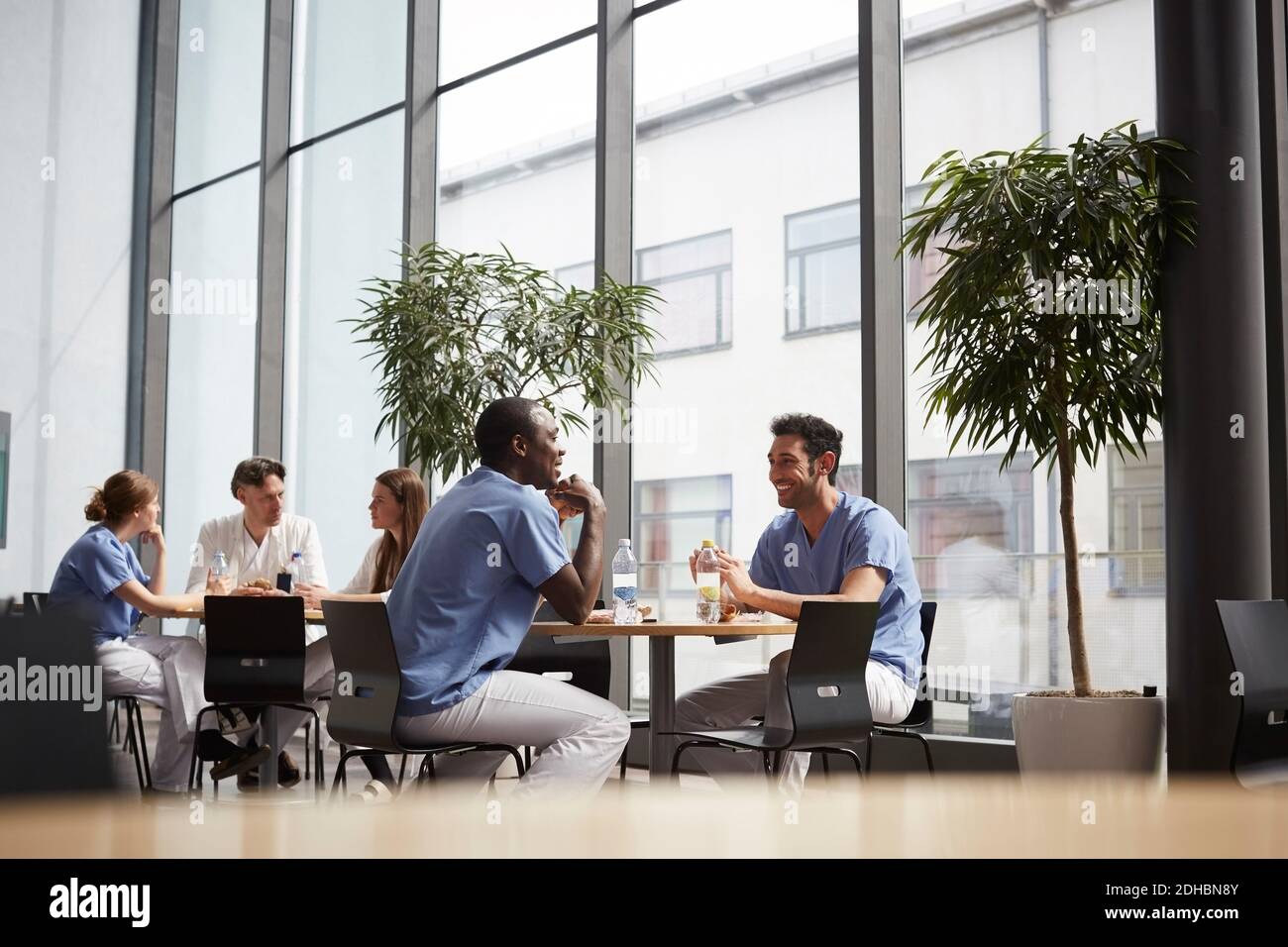 Équipe médicale multiethnique souriante assise à la cafétéria de l'hôpital Banque D'Images