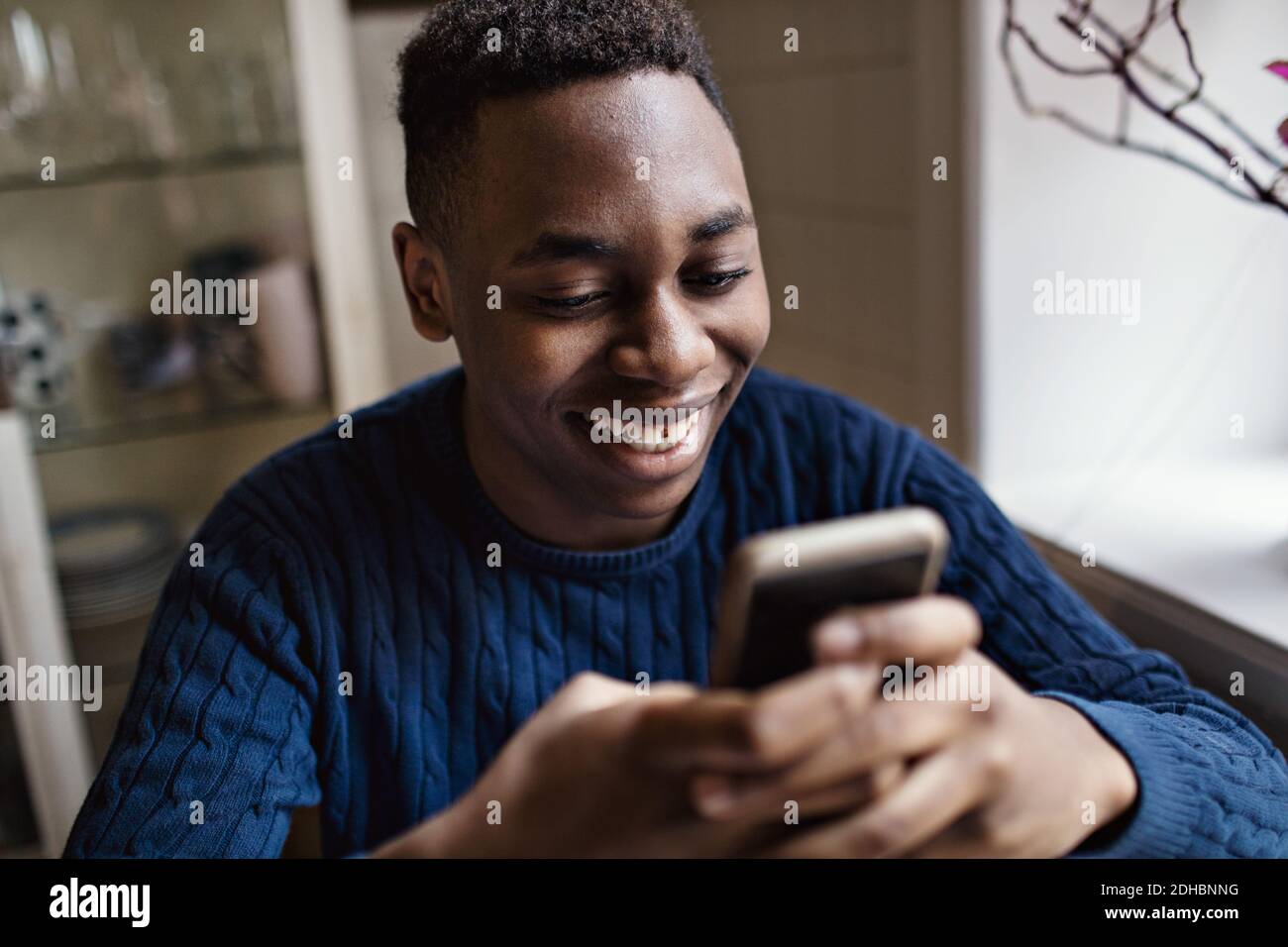 Jeune garçon souriant utilisant un smartphone tout en étant assis à la maison Banque D'Images
