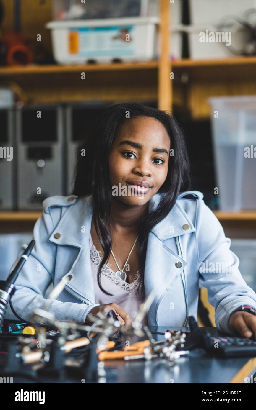 Portrait d'une femme souriante étudiante du secondaire assise avec la science projection au bureau en salle de classe Banque D'Images