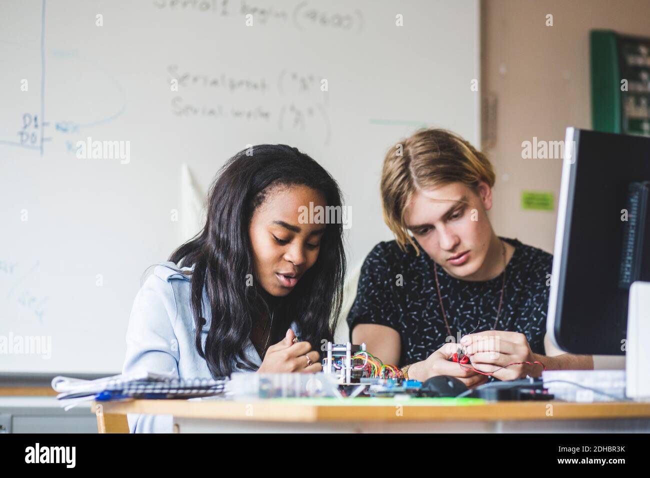 Étudiante confiante préparant un projet scientifique avec un jeune ami masculin sur le bureau dans la salle de classe à l'école secondaire Banque D'Images