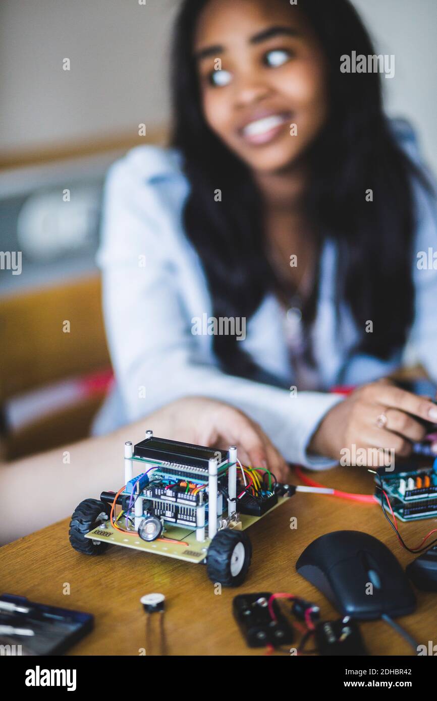 Un étudiant souriant assis par un ami avec une voiture-jouet sur le bureau en classe à l'école secondaire Banque D'Images