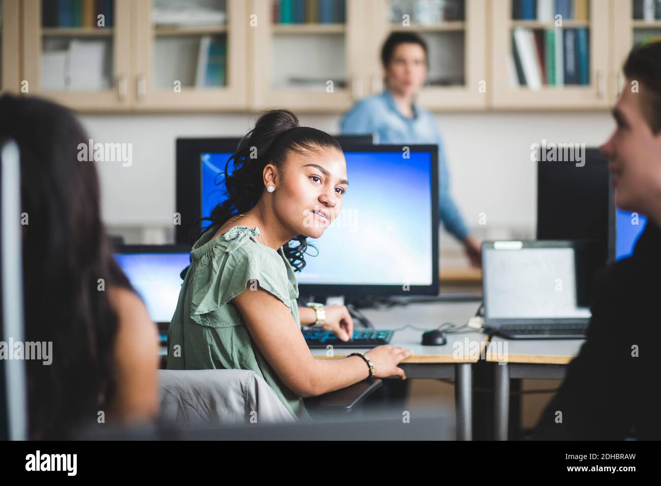 Une étudiante de lycée confiante qui regarde un ami assis laboratoire informatique Banque D'Images