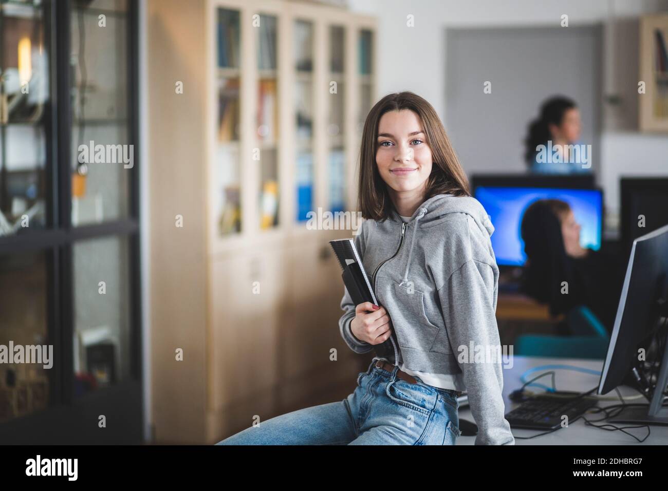 Portrait d'une étudiante de lycée souriante assise avec des livres sur le bureau en classe Banque D'Images
