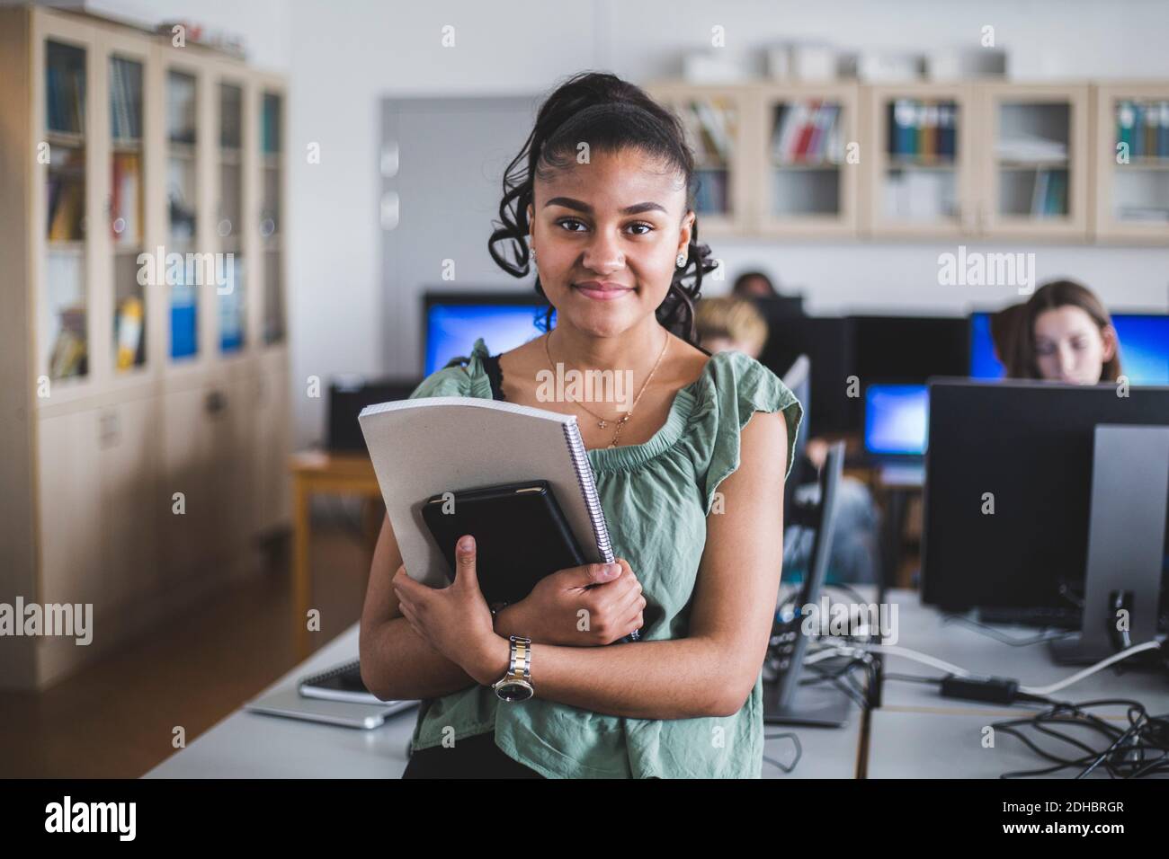 Portrait d'une adolescente souriante debout avec livre dans un ordinateur laboratoire à l'école secondaire Banque D'Images
