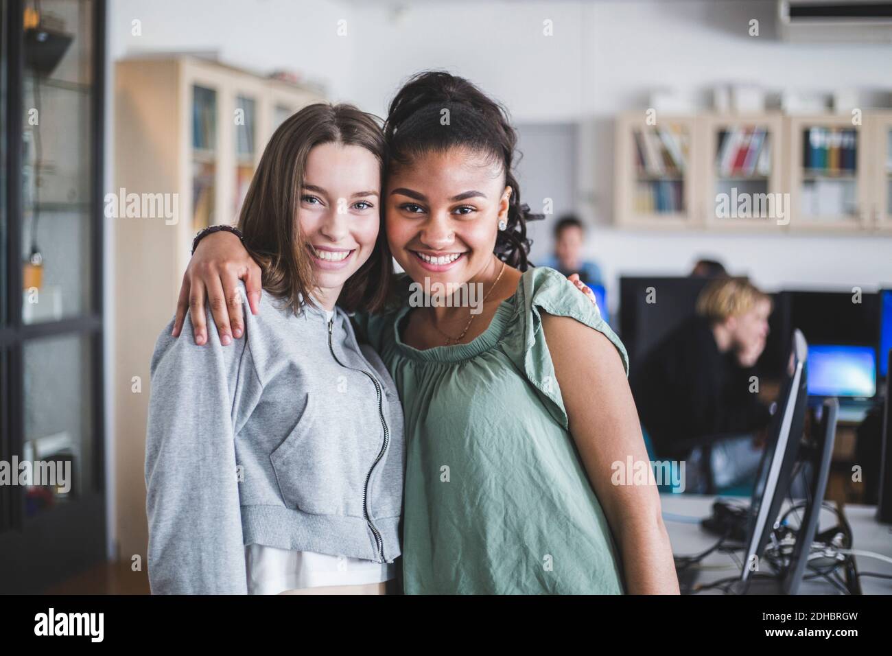 Portrait d'adolescentes souriantes debout avec le bras autour en laboratoire informatique à l'école secondaire Banque D'Images