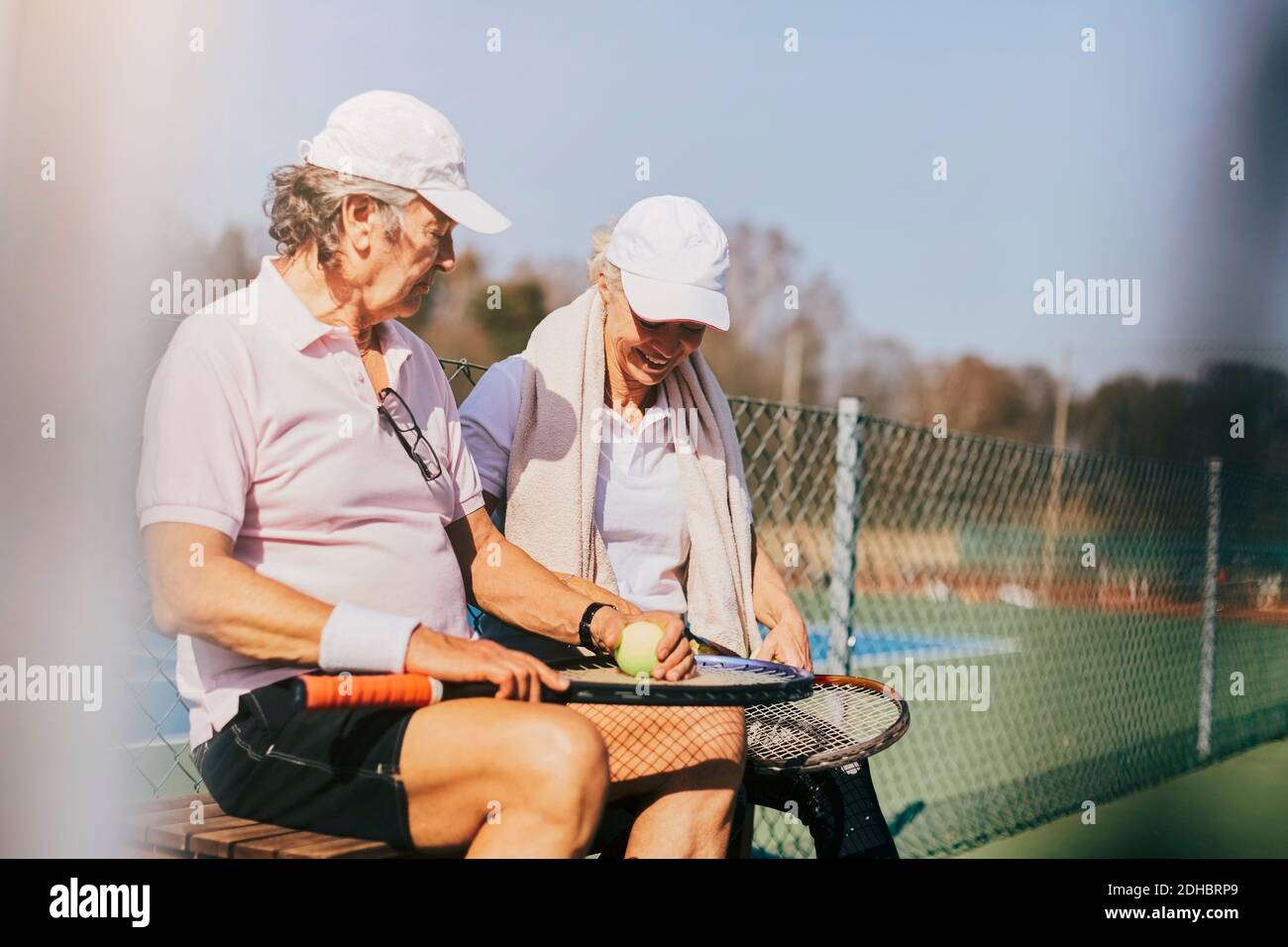 Des amis masculins et féminins de haut niveau parlent en étant assis sur le banc au cour en été Banque D'Images