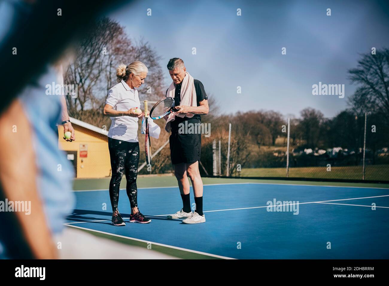 Homme et femme senior avec des raquettes parlant en se tenant à court de tennis Banque D'Images