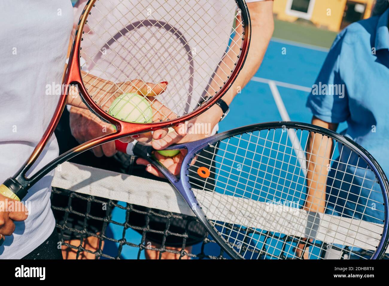 Mi-section d'amis tenant une balle de tennis et des raquettes en se tenant debout au tribunal Banque D'Images