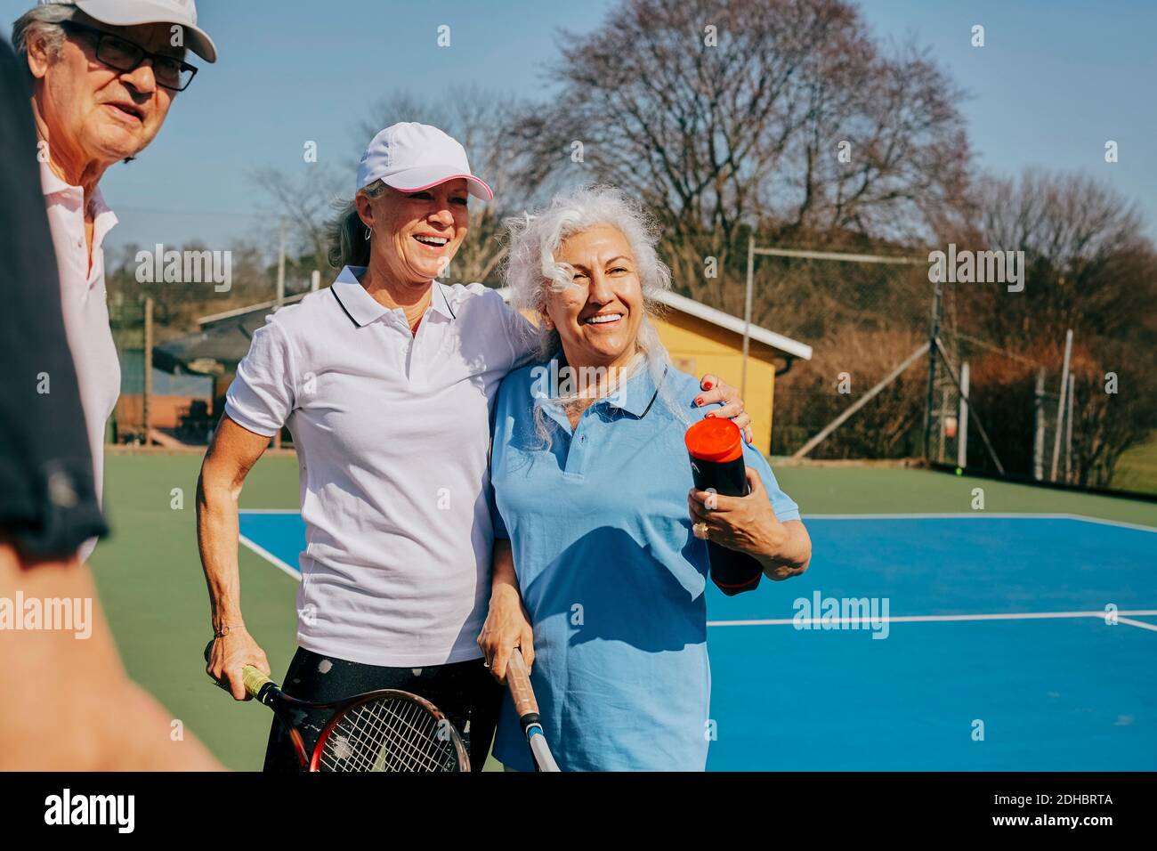 De joyeux amis âgés qui regardent loin tout en tenant une raquette de tennis à cour Banque D'Images