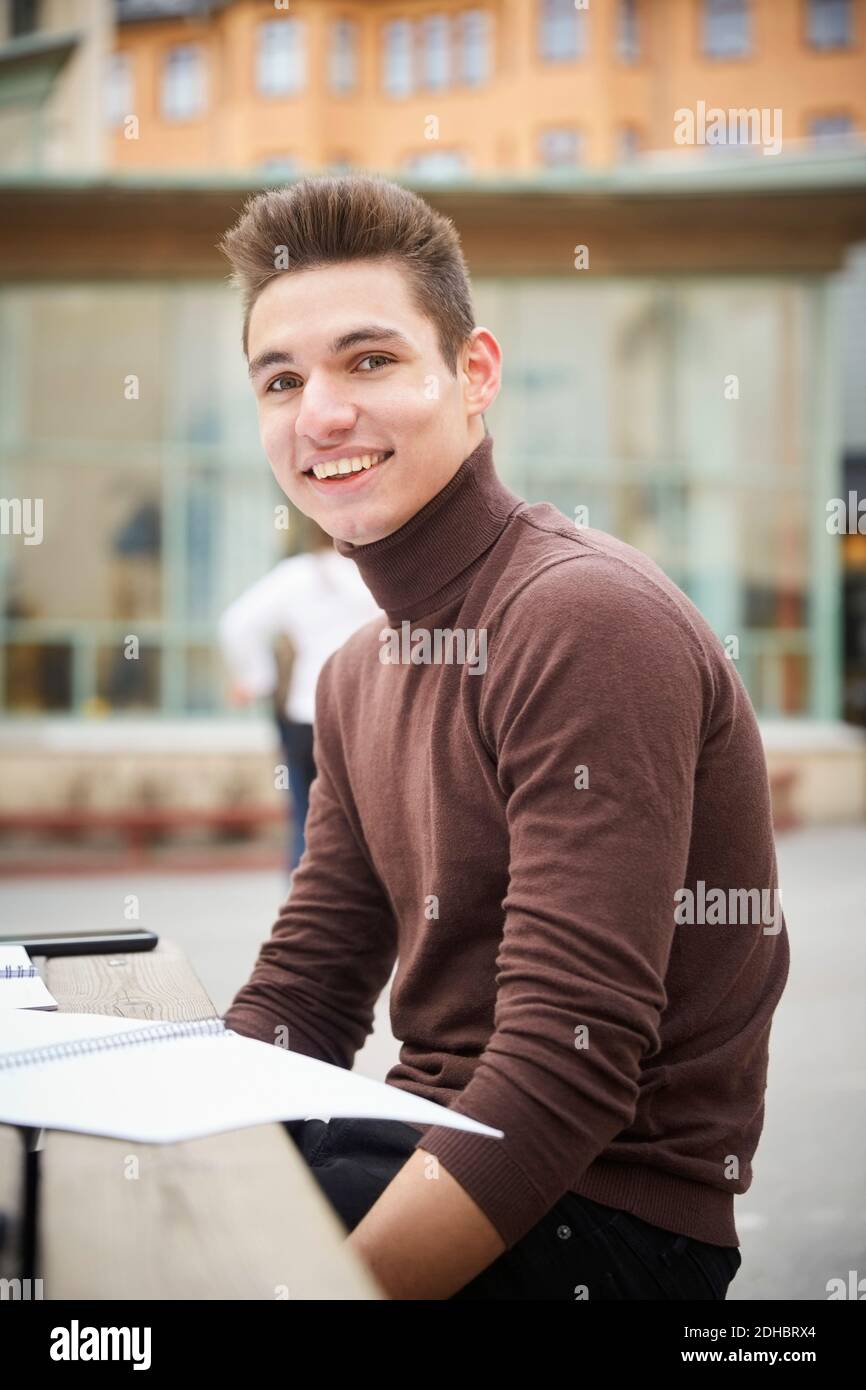 Portrait d'un adolescent souriant assis à table dans la cour d'école Banque D'Images