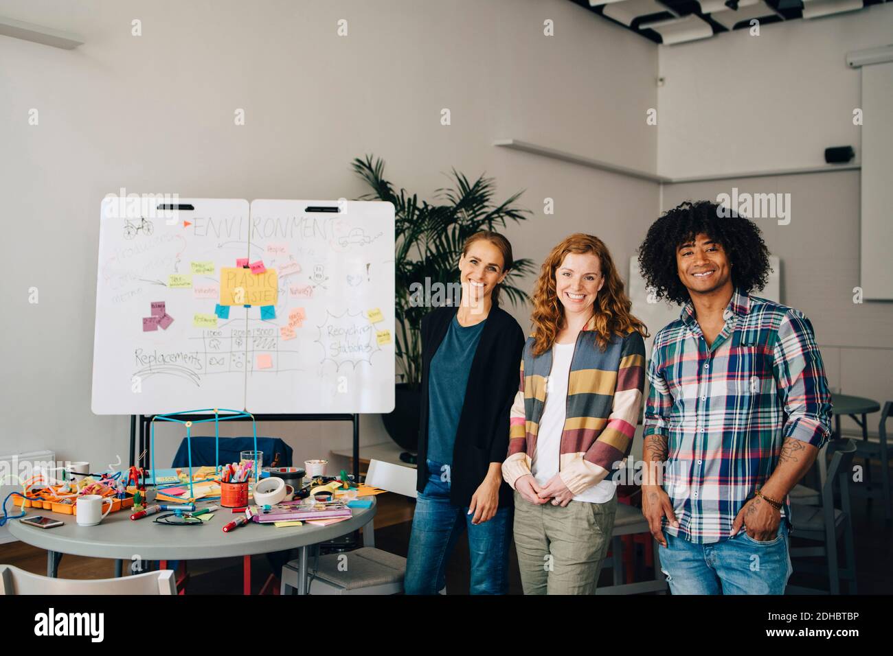 Portrait d'une équipe de techniciens souriants debout sur une table et un tableau blanc au bureau de création Banque D'Images