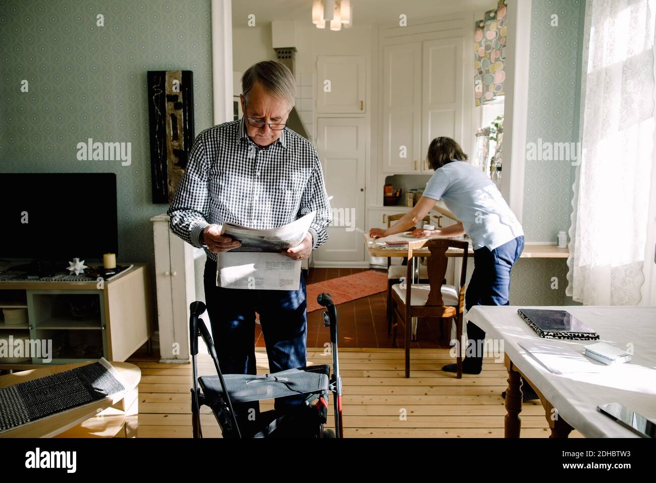 Un homme âgé à la retraite lisant un journal alors qu'une femme travaillait chez elle cuisine à la maison de soins Banque D'Images