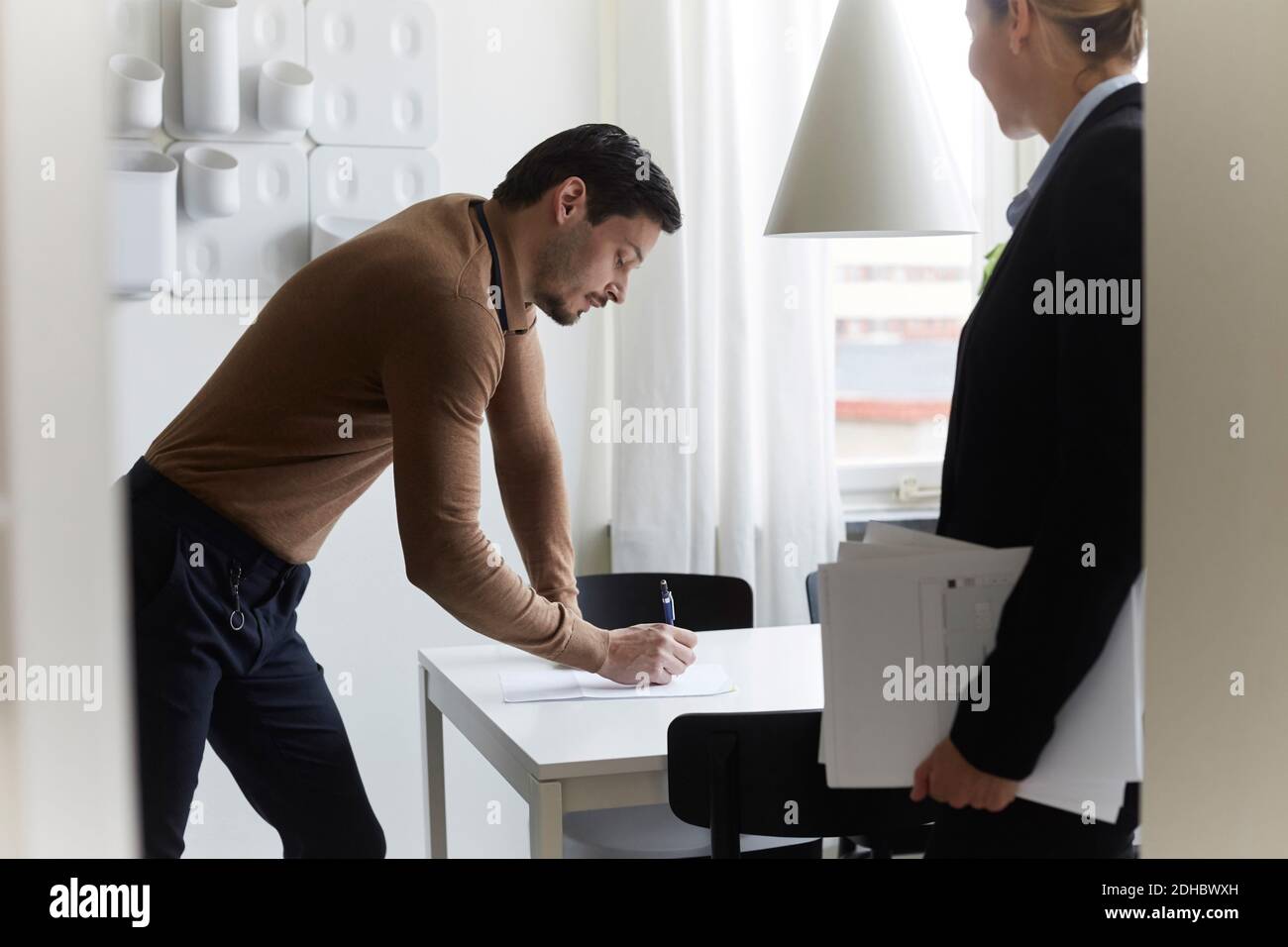 Homme de taille moyenne signant le document lorsqu'il est debout dans l'immobilier agent à la nouvelle maison Banque D'Images