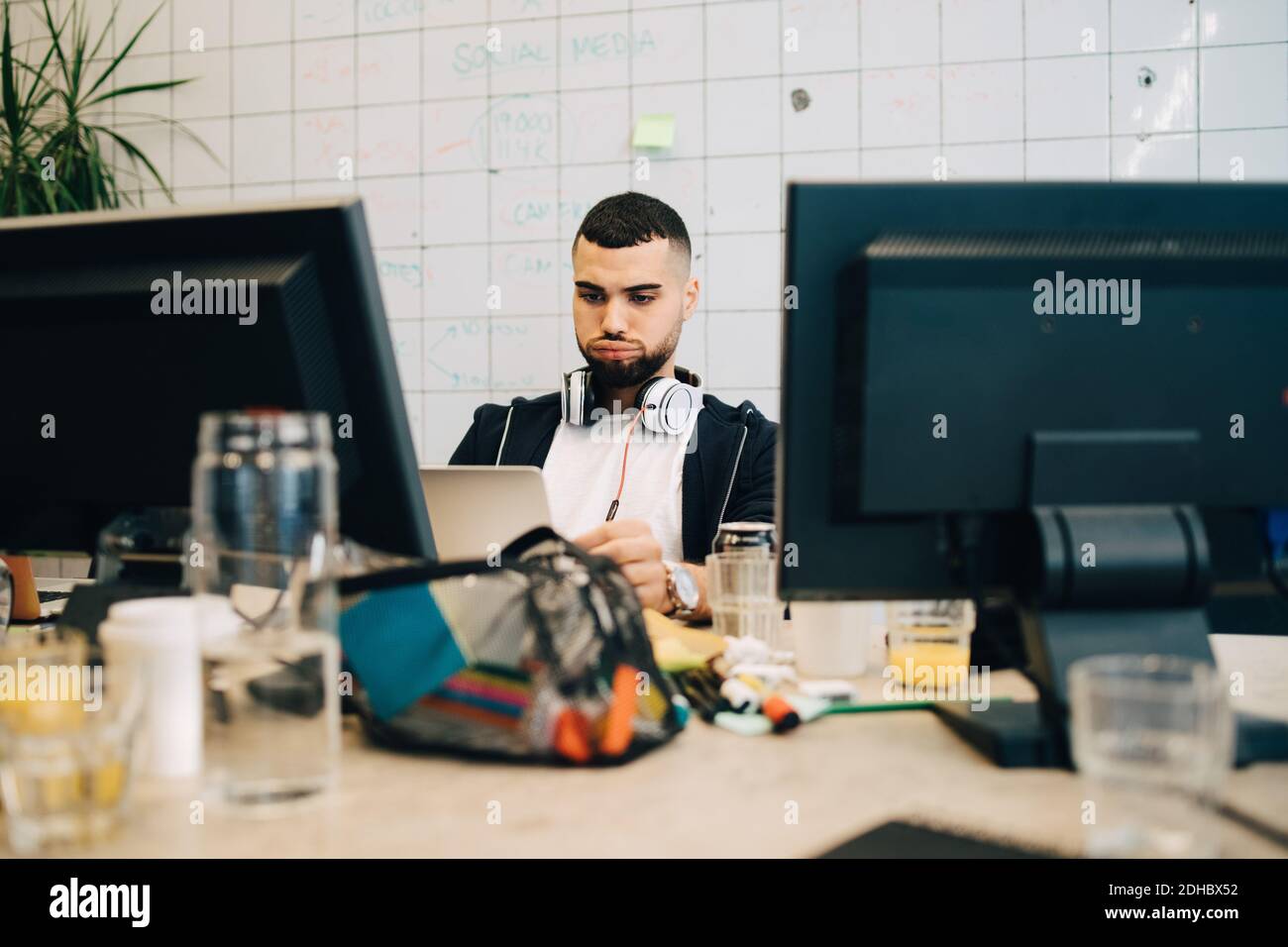 Jeune homme hacker d'ordinateur faire le visage tout en encodant sur ordinateur portable au bureau de création Banque D'Images