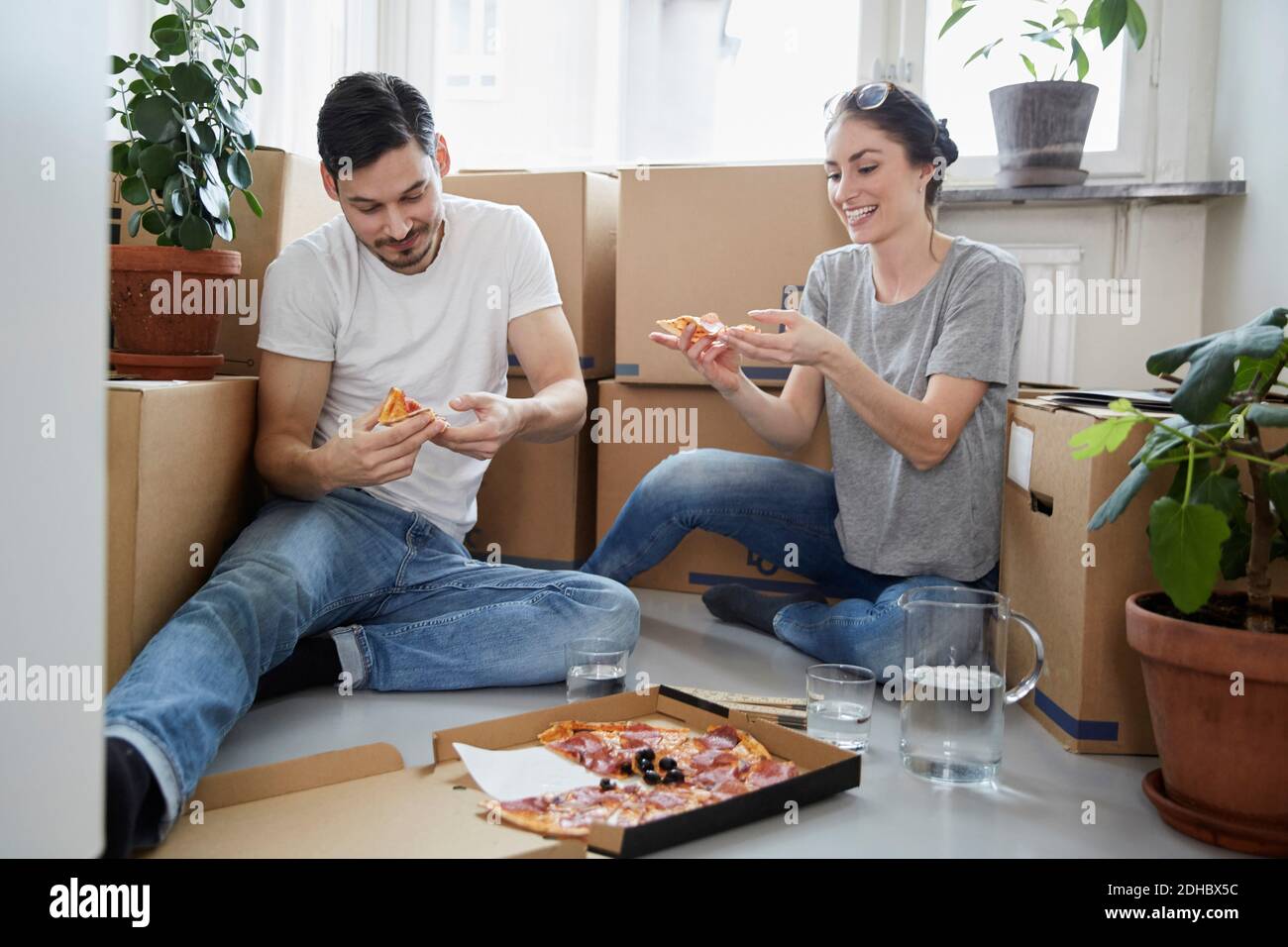 Couple souriant qui mange de la pizza tout en étant assis contre des boîtes en carton nouvelle maison Banque D'Images
