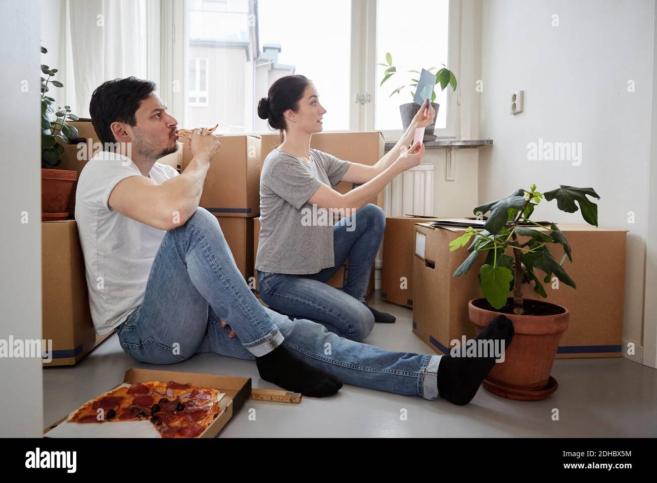 Homme mangeant de la pizza tout en regardant la femme choisissant des nuances de couleur dans une nouvelle maison Banque D'Images