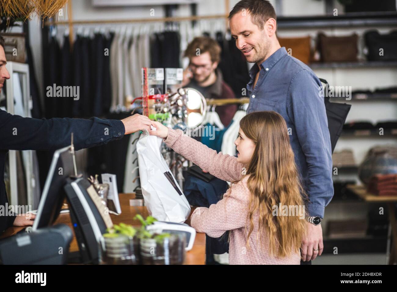 Vue latérale de la fille qui reçoit le sac de magasinage du caissier père au comptoir de caisse dans le magasin de vêtements Banque D'Images