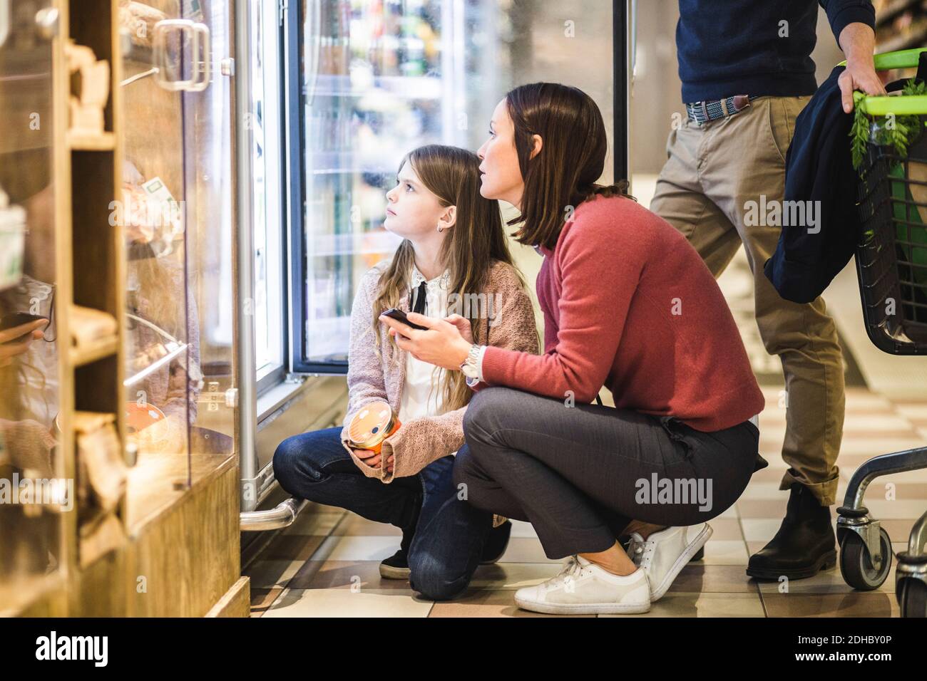 Pleine longueur de la mère et de la fille regardant dans le réfrigérateur pendant accroupi au supermarché Banque D'Images