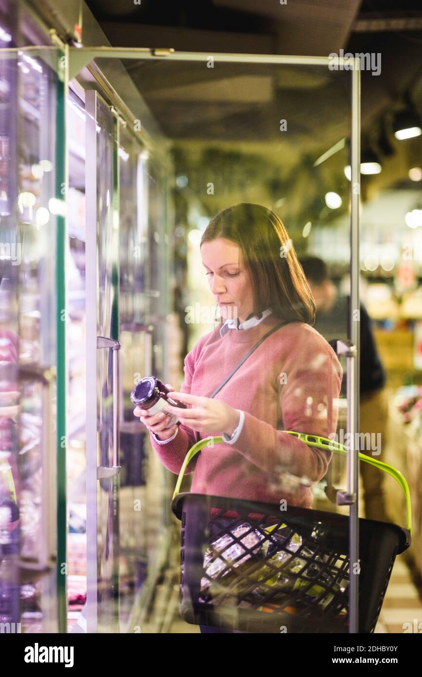Une femme mature fait ses courses en se tenant près d'un réfrigérateur dans un supermarché Banque D'Images