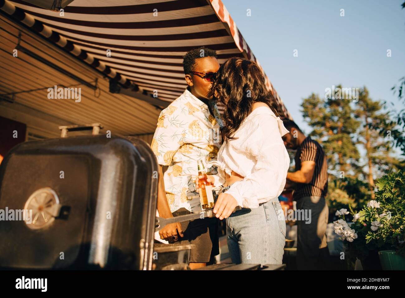 Petite amie embrassant petit ami en se tenant près du barbecue en fête Banque D'Images