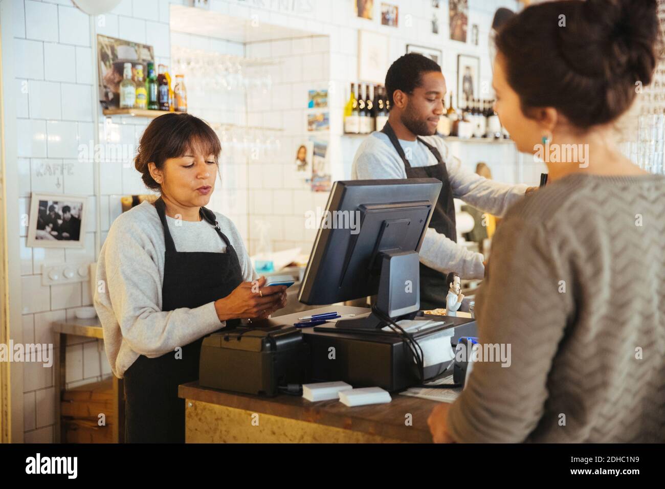 Une femme mature qui facture un client se tenant au comptoir de caisse épicerie fine Banque D'Images