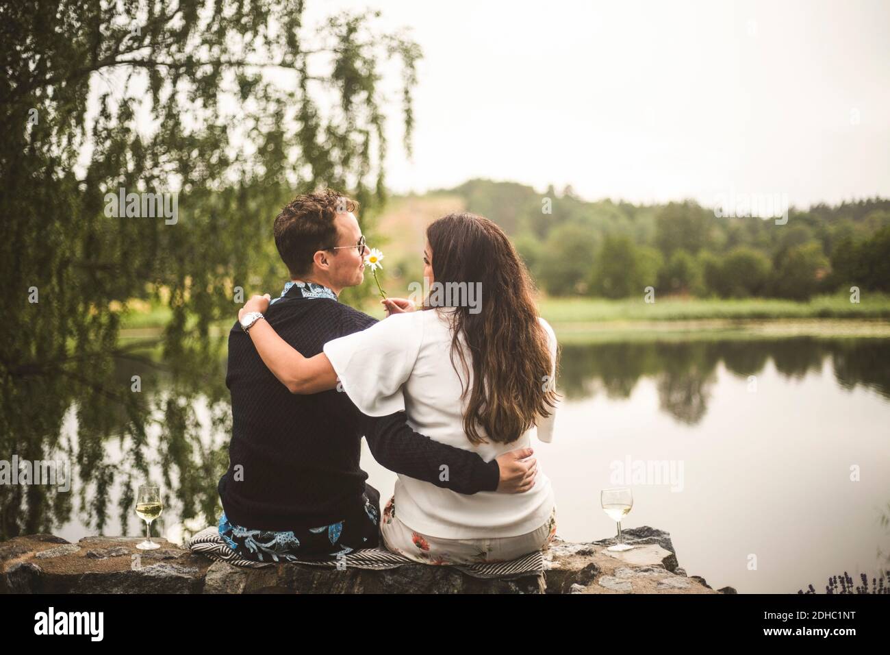 Vue arrière d'un couple romantique assis sur le mur de soutènement contre lac Banque D'Images