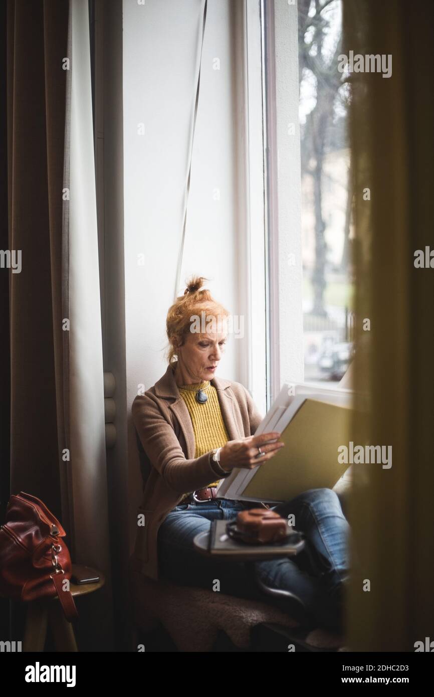 Femme d'âge mûr, assise avec papiers sur le rebord de la fenêtre bureau Banque D'Images