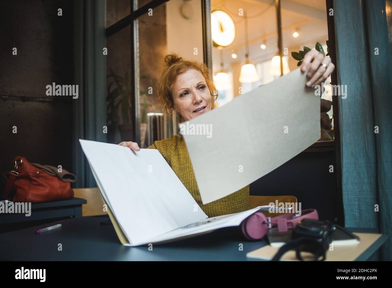 Illustratrice femme confiante et mature tenant des papiers au bureau dans un esprit créatif bureau Banque D'Images