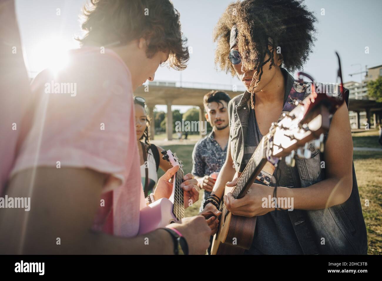 Amis regardant des hommes jouant ukulele en concert sur ensoleillé jour Banque D'Images