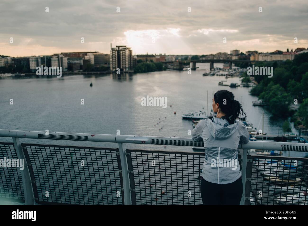 Vue arrière d'une athlète féminine qui regarde la ville en se tenant debout sur la passerelle au-dessus de la mer pendant le coucher du soleil Banque D'Images