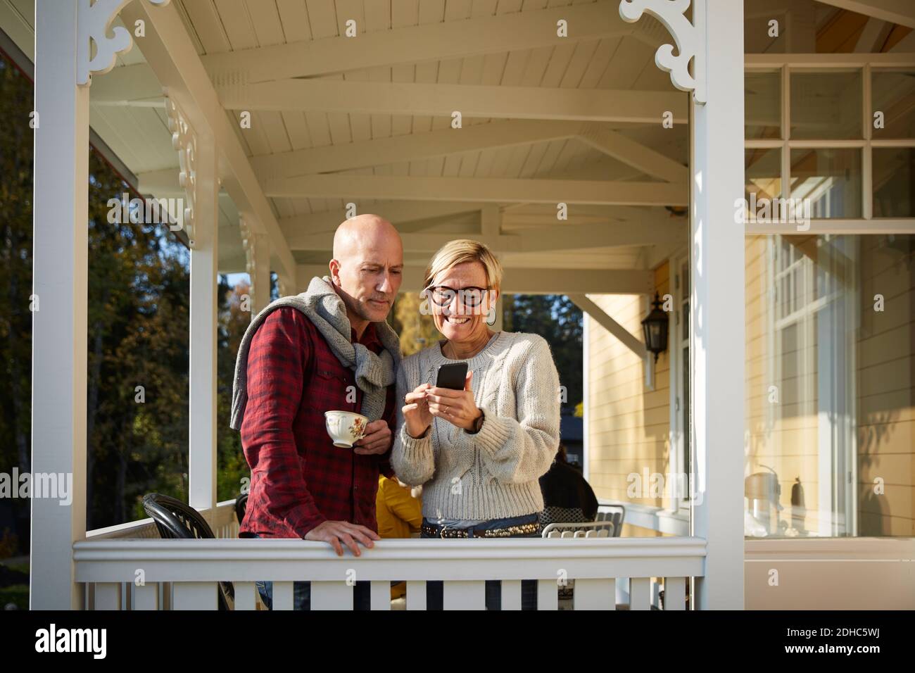 Femme mûre souriante montrant le téléphone portable à un ami chauve pendant sur le porche Banque D'Images