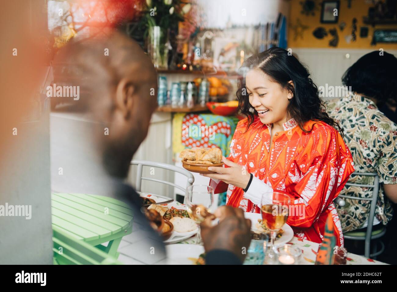Une jeune femme souriante mange un déjeuner avec un ami assis à table dans le restaurant vu par la fenêtre Banque D'Images