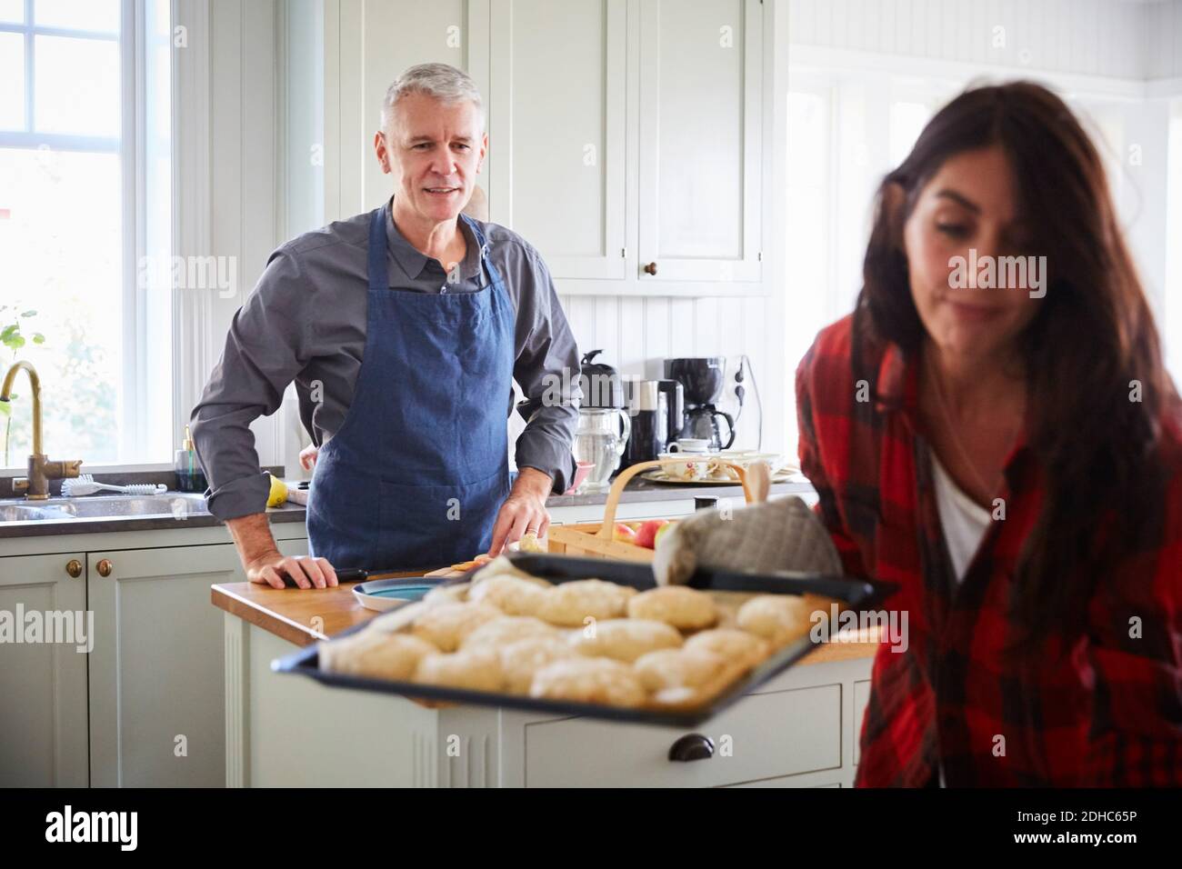 Homme mûr souriant regardant une femme tenant une plaque de cuisson cuisine Banque D'Images