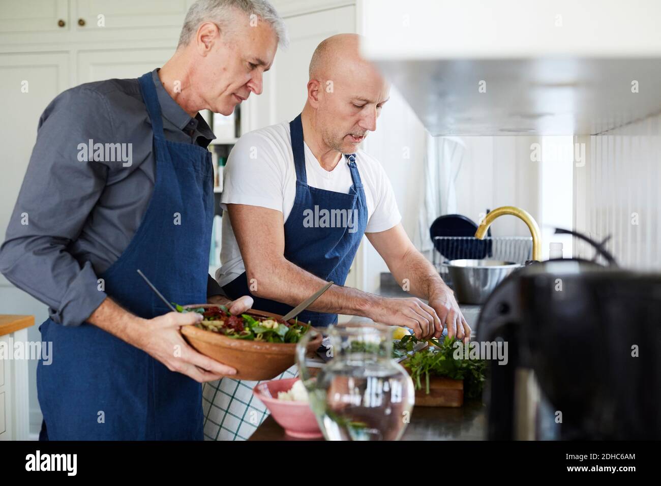 Des hommes matures parlent tout en cuisinant des aliments dans la cuisine à la maison Banque D'Images