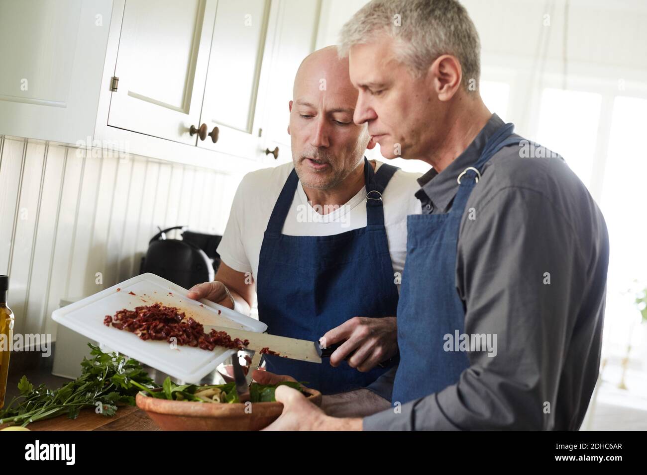 Homme à tête blanche et mature aidant un ami à cuisiner des aliments à la maison Banque D'Images