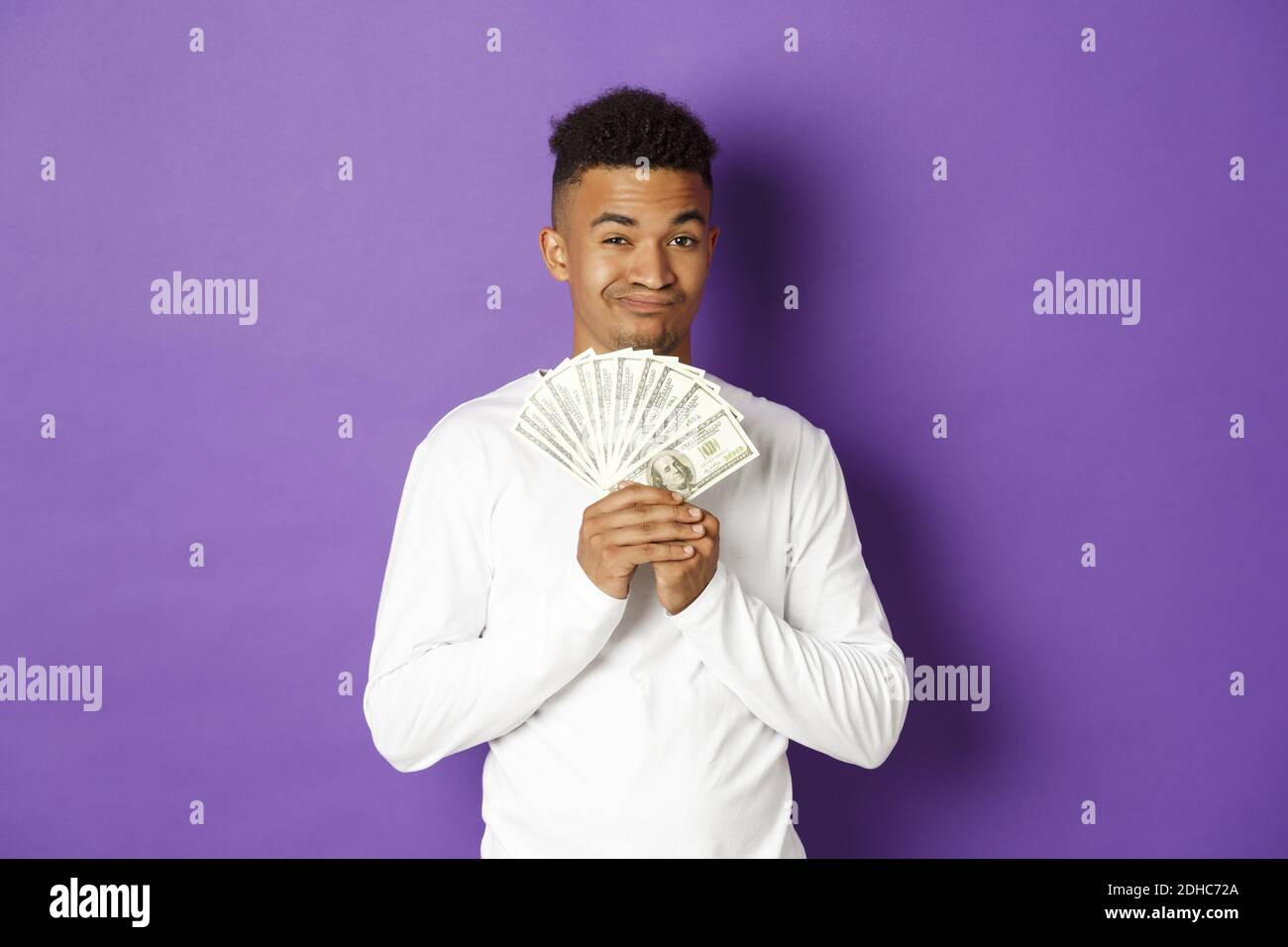 Un gars afro-américain méchant, qui se vante et montre une grosse somme d'argent, qui gagne à la loterie ou qui a obtenu un prêt, se tenant sur fond violet Banque D'Images