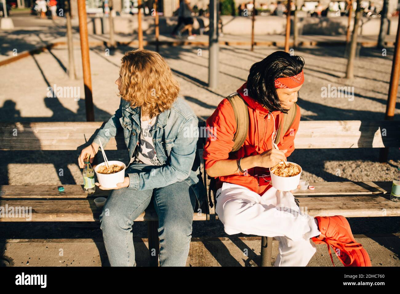 Des amis qui mangent à emporter de la nourriture tout en étant assis sur le banc à l'intérieur ville pendant la journée ensoleillée Banque D'Images