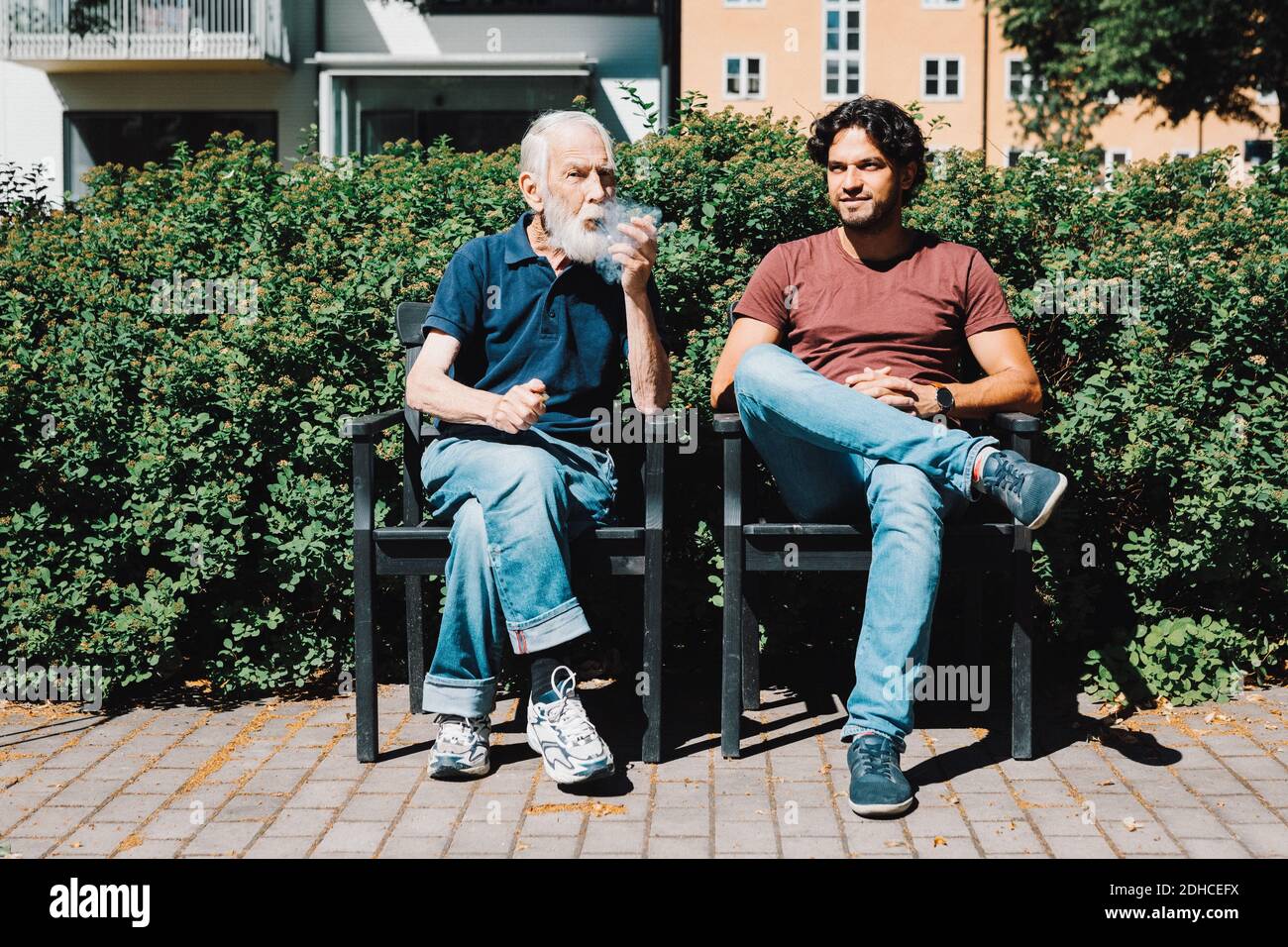 Pleine longueur de l'homme âgé à la retraite fumant pipe pendant assis avec gardien mâle contre maison de soins Banque D'Images