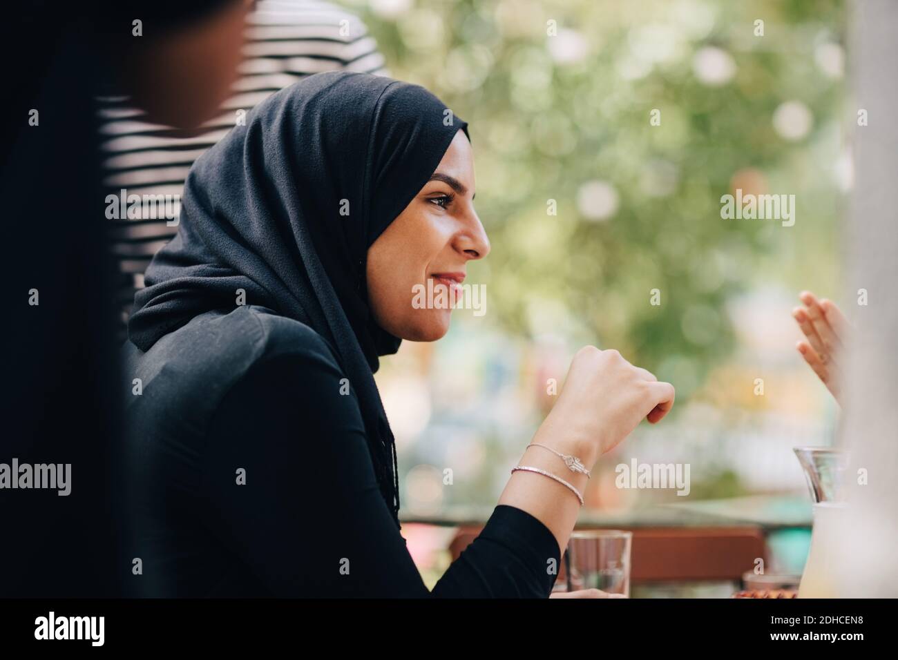 Jeune femme dans hijab regardant loin en s'asseyant au balcon pendant la fête Banque D'Images