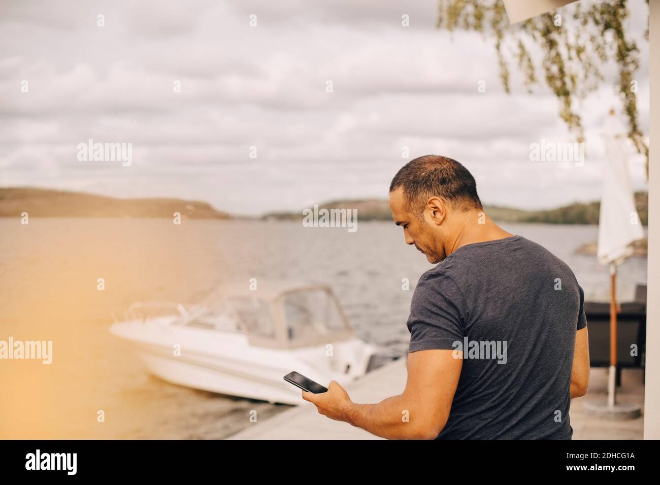 Homme mature utilisant un smartphone avec yacht amarré sur le lac en arrière-plan Banque D'Images